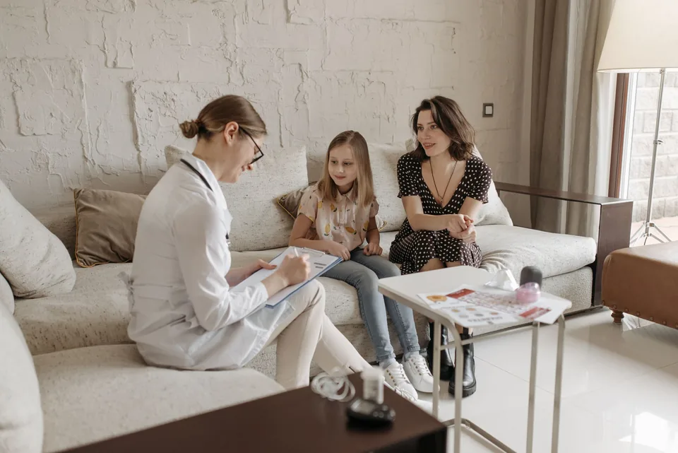 Mãe e filha sorrindo no sofá enquanto conversam com a médica